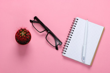 Notebook with pen, glasses, cactus on pink pastel background. Working space. Top view