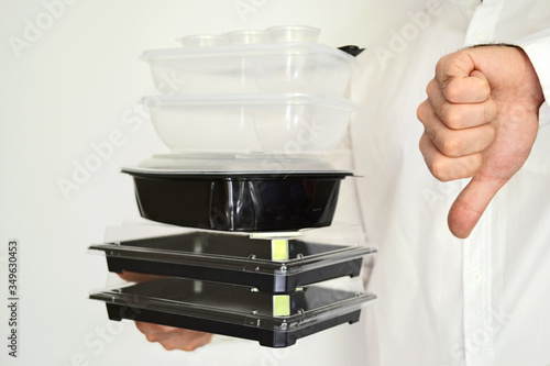Man holds empty plastic food boxes in his hands and shows thumb down on a white background. The concept of reasonable consumption. Recycling.