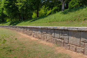 Wall Mural - Long low rusticated stone block retaining wall in an outdoor park, green hillside and trees beyond, horizontal aspect