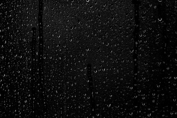 Drops of water flow down the surface of the clear glass on a black background. Texture for creativity.