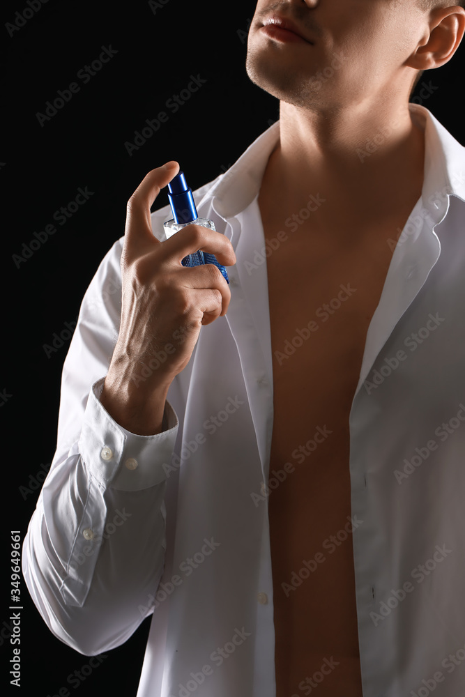 Handsome young man with bottle of perfume on dark background