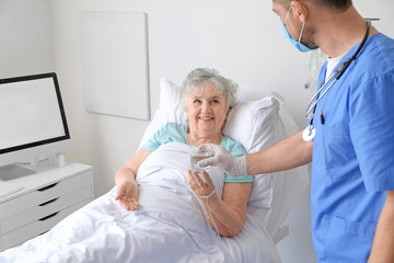 Wall Mural - Male doctor working with elderly patient in hospital room