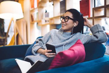 Cheerful Asian woman lounging on sofa with mobile phone