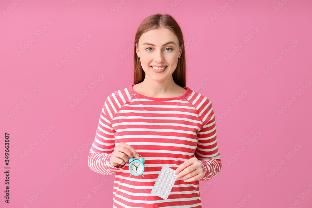 Young woman with birth control pills and clock on color background