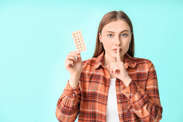 Sticker - Young woman with birth control pills showing silence gesture on color background