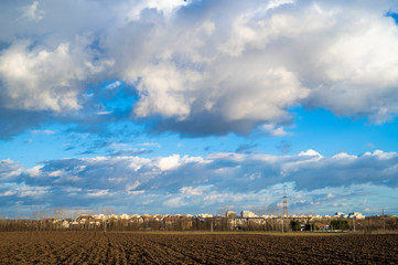 Landscape of a field outside of the city. Block of flats in the background. Beautiful painting-like clouds in the blue sky. 