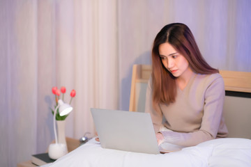 A beautiful woman with long hair. Asian people. Thai people wear long-sleeved shirts sitting and typing the keyboard on the laptop on the bed in the bedroom. with copy space