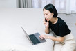 © Gengwit - Attractive asian female calling with co-worker while working with laptop. at home Work from home concept.