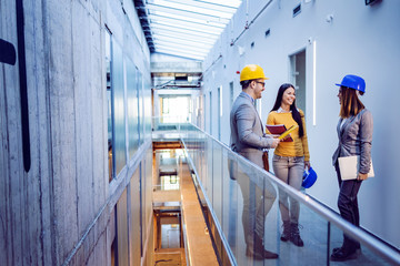 Wall Mural - Three smiling positive hardworking caucasian architects standing in building in construction process and talking how they want to rebuild it to be modern.