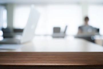 Empty wooden desk space over blurred office or meeting room background. Product display.