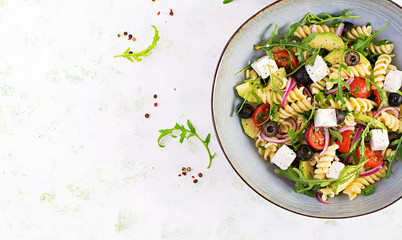 Wall Mural - Pasta salad with tomato, avocado, black olives, red onions and cheese feta. Mediterranean cuisine. Top view, overhead, flat lay