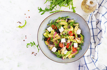 Pasta salad with tomato, avocado, black olives, red onions and cheese feta. Mediterranean cuisine. Top view, overhead, flat lay