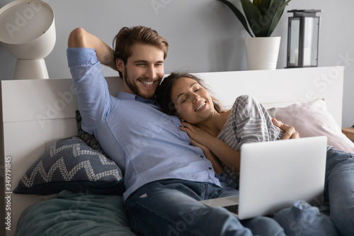 Photographie Happy young Caucasian couple lying relaxing in comfortable bed watching video on