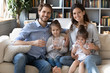 © fizkes - Portrait of happy young Caucasian family with little daughters on couch at home recommend drinking water, smiling parents with small girls children follow healthy lifestyle, dieting, wellness concept