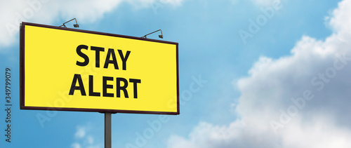 Stay Alert yellow warning sign on blue sky background. Large billboard with the message text. Staying alert after easing coronavirus lockdown restrictions; end of Covid-19 quarantine concept