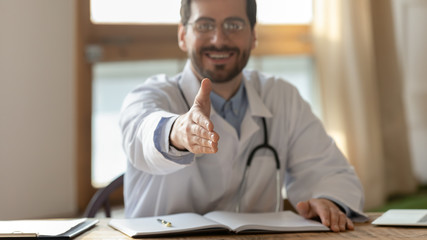 Close up focus portrait of smiling male doctor in whites stretch hand greeting with patient or client at consultation, man GP get acquainted with customer at meeting in hospital, healthcare concept