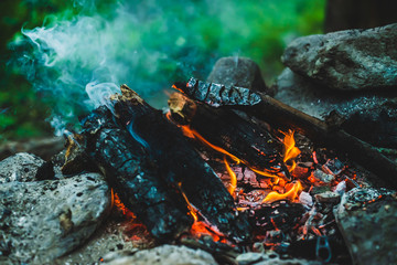 Vivid smoldered firewoods burned in fire close-up. Atmospheric warm background with orange flame of campfire and blue smoke. Wonderful full frame image of bonfire. Burning logs in beautiful fire.