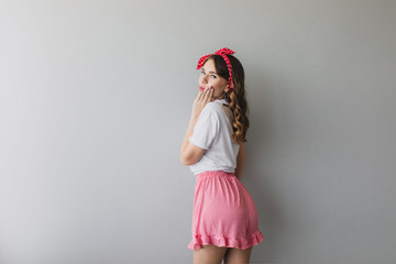 Wall Mural - Portrait of romantic lady in pajamas looking over shoulder. Indoor photo from back of curly girl in pink shorts.