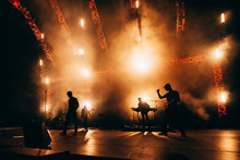 Сoncert Of Popular Group. Musicians Silhouette. Rock Band Performs On Stage. Guitarist, Bass Guitar, Keyboard Player And Drums. Bright Light Show At The Stadium.
