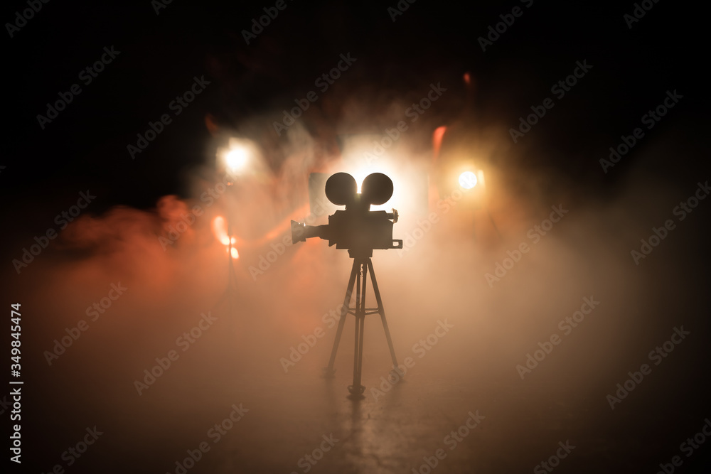 Movie concept. Miniature movie set on dark toned background with fog and empty space. Silhouette of vintage camera on tripod. - obrazy, fototapety, plakaty 