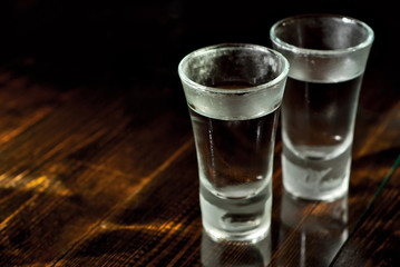 Two frozen glasses close up. Glasses with alcohol on a black wooden table. Vodka on a dark contrasting background.