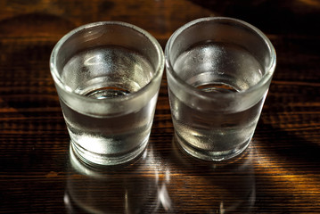 Two frozen glasses close up. Glasses with alcohol on a black wooden table. Vodka on a dark contrasting background.