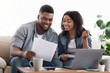 © Prostock-studio - Black couple reading financial documentation at home while planning family budget