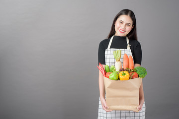 Wall Mural - Portrait of beautiful young woman with vegetables in grocery bag in studio grey background