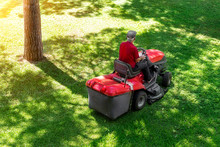Top Down Above View Of Professional Lawn Mower Worker Cutting Fresh Green Grass With Landcaping Tractor Equipment Machine At City Park. Garden And Backyard Landscape Lawnmower Service And Maintenance