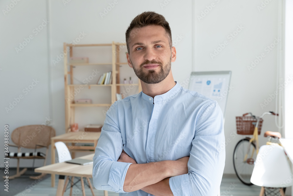 Close up head shot portrait picture of smiling businessman crossing hands looking at camera. Happy confident millennial man manager on workplace background in office. - obrazy, fototapety, plakaty 