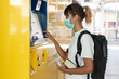 © DUSITARA STOCKER - Asian woman with surgical face mask feel tired using ticket machine for travel by subway or skytrain, carrying backpack, traveling to the city, social distancing, coronavirus, COVID19