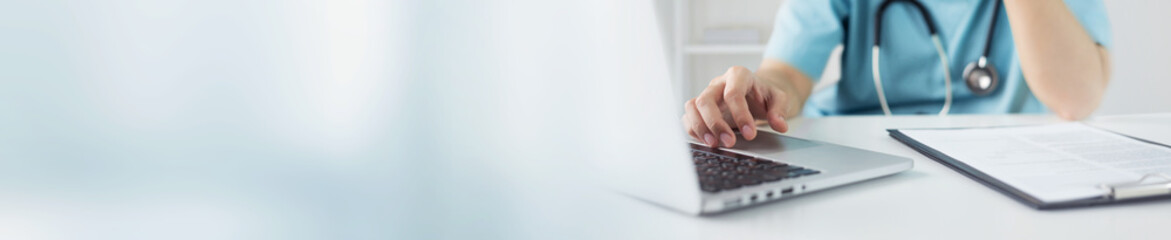 Asian Doctor or nurse in blue uniform concentrate working on laptop computer and preparing information of patients for meeting with medical team in hospital. Selective focus on hand. Banner, web