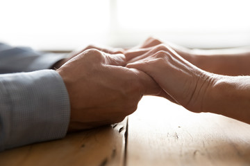 Side close up view older loving husband holding wrinkled hands of senior woman, supporting at hard time. Middle aged mature family married couple showing love understanding, giving psychological help.