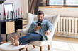 © fizkes - Millennial Caucasian man sit relax in armchair in modern design living room use cellphone, focused young male in glasses rest in comfortable chair at home browsing Internet on smartphone device