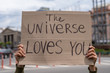Positive thinking supportive message from the Universe loves you.  Hands holding banner outside on city streets. social care motivation concept. Friendly mood attitude. Self-love message. Loves you