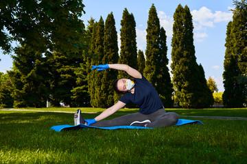 Girl doing yoga and stretching in the park outdoors in a protective mask and gloves. Quarantine time in coronavirus epidemic, social constraints