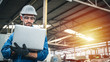 © Pitchayaarch - Confident engineer in blue jumpsuit holding laptop computer in a warehouse.