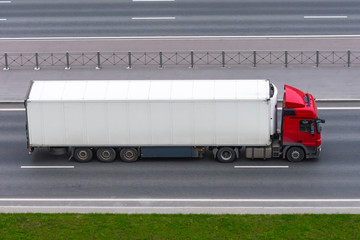 Wall Mural - Truck with a white container on a trailer rides on a city highway, aerial side view.