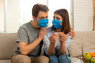 Couple in masks sitting on couch in room