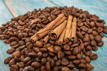 Cinnamon lies roasted coffee beans on a blue wooden background.