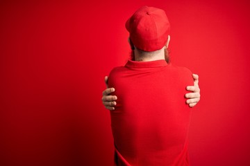 Wall Mural - Young handsome delivery man wearing glasses and red cap over isolated background Hugging oneself happy and positive from backwards. Self love and self care