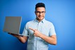 © Krakenimages.com - Young handsome businessman wearing glasses working using laptop over blue background very happy pointing with hand and finger