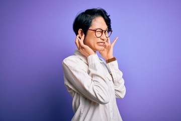 Poster - Young beautiful asian girl wearing casual shirt and glasses standing over purple background covering ears with fingers with annoyed expression for the noise of loud music. Deaf concept.