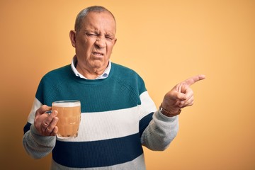 Sticker - Senior handsome man drinking jar of beer standing over isolated yellow background Pointing aside worried and nervous with forefinger, concerned and surprised expression