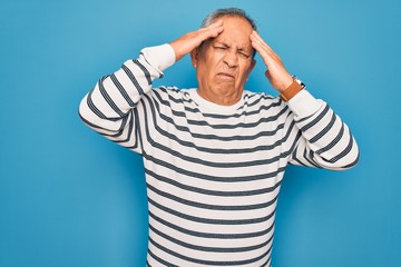 Wall Mural - Senior handsome grey-haired man wearing striped sweater over isolated blue background suffering from headache desperate and stressed because pain and migraine. Hands on head.