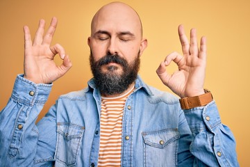 Sticker - Handsome bald man with beard wearing casual denim jacket and striped t-shirt relax and smiling with eyes closed doing meditation gesture with fingers. Yoga concept.