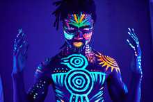 Portrait Of African Man Painted In Fluorescent Paint On Face And Muscular Torso, Studio Shot With UV Light. Ethnic Prints