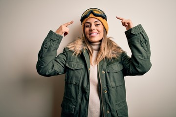 Canvas Print - Young brunette skier woman wearing snow clothes and ski goggles over white background smiling pointing to head with both hands finger, great idea or thought, good memory