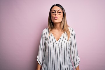 Poster - Young beautiful woman wearing casual striped t-shirt and glasses over pink background looking at the camera blowing a kiss on air being lovely and sexy. Love expression.