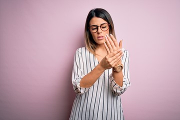 Wall Mural - Young beautiful woman wearing casual striped t-shirt and glasses over pink background Suffering pain on hands and fingers, arthritis inflammation